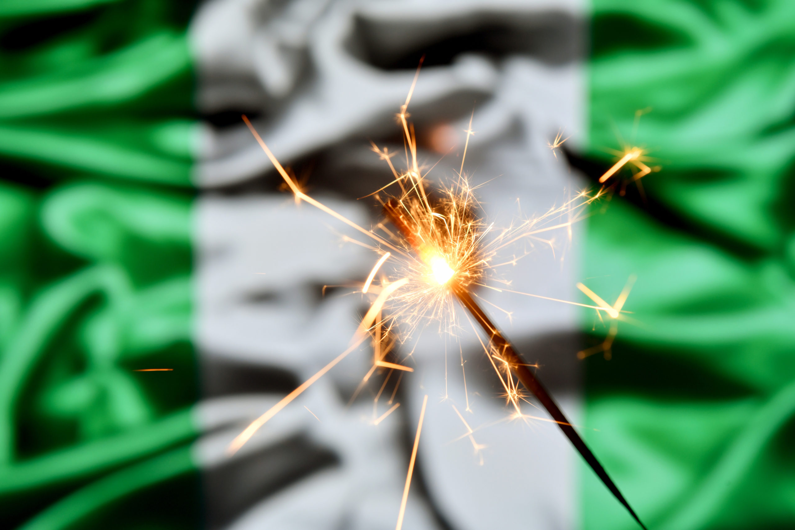 Close up of sparkler burning over Nigerian flag.